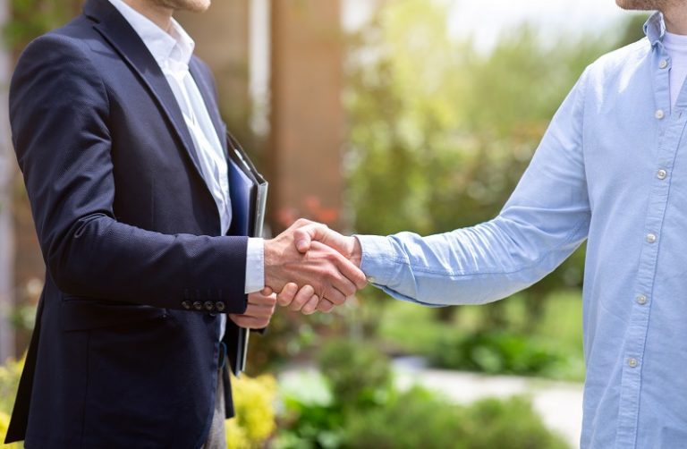 Closeup view of real estate agent and his client shaking hands near new house